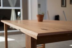 a wooden table with a potted plant sitting on it's end, in front of a window