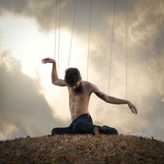 a shirtless man sitting on top of a hill holding onto strings with his hands