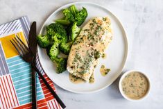 a white plate topped with chicken and broccoli next to a bowl of sauce