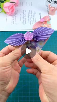 someone is holding a purple paper flower in their hands and making it look like an origami butterfly