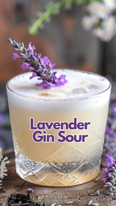 the lavender gin sour is sitting on top of a piece of wood next to flowers