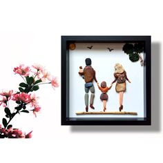 an image of a family holding hands with flowers in the foreground and behind it is a shadow box