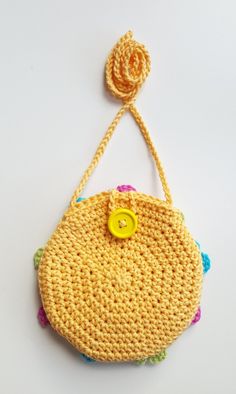 a crocheted purse with a yellow button hanging from it's side on a white surface