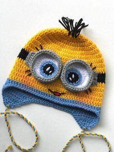 a crocheted hat with two eyes and a string on the bottom that is yellow and blue