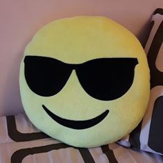 a smiley face pillow with sunglasses on it's head sitting next to a black and white pillow