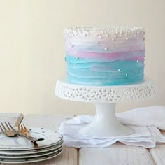 there is a cake with blue, pink and white frosting on it next to plates