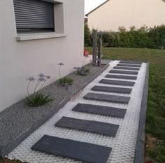 an outdoor walkway made out of stones and gravel in front of a white building with blue flowers on the side