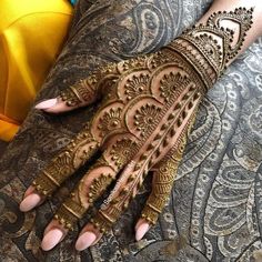 henna on the hands of a woman with intricate patterns and gold decorations, showing off her hand