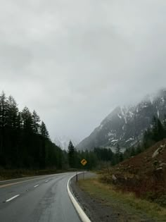 an empty road in the mountains with snow on the top and evergreen trees around it