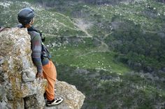 a man standing on top of a cliff next to a lush green valley