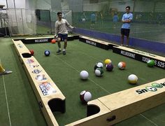 two men are playing ping pong on an indoor court with several balls scattered about