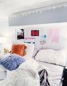 a white bed topped with lots of pillows next to a night stand and lights on the wall