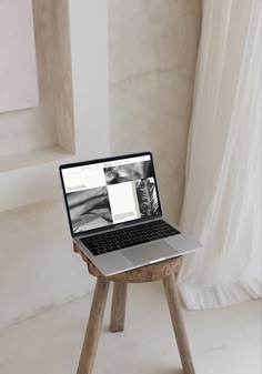 an open laptop computer sitting on top of a wooden stool in front of a window