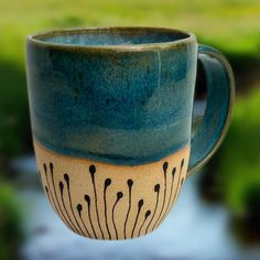 Bring a touch of nature to your morning routine with our handcrafted Creekside Sips Mug. Inspired by tranquil creekside mornings, this ceramic mug features a soothing blue glaze and rustic clay reminiscent of water meeting earth. The intricate, organic design at the base adds a whimsical, nature-inspired touch, making each sip feel like a breath of fresh air. Amply sized (14 fl. oz.) for your favorite coffee, tea, or cocoa, this mug is both a practical and decorative addition to your kitchen. Wh Whimsical Nature, Glaze Ideas, Pottery Glaze, Unique Pottery, Cozy Mornings, Pottery Glazes, Organic Design, Handcrafted Ceramics, Breath Of Fresh Air