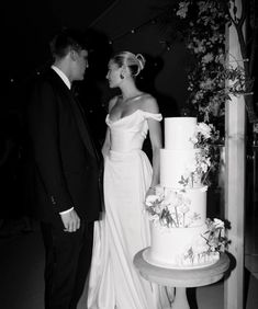 a man and woman standing in front of a wedding cake with flowers on the side