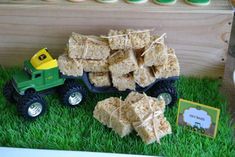 a toy truck filled with rice krispy treats sitting on top of green grass next to cupcakes