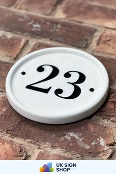 a white sign with the number 23 on it sitting on a brick floor next to a brick wall