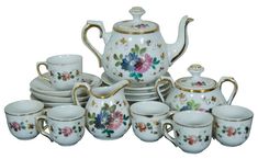 a white tea set with floral designs and gold trimmings on the top, surrounded by other cups and saucers