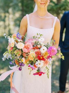 a bride holding a bouquet of flowers in her hand and a groom standing behind her