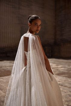 a woman in a white wedding dress with a veil on her head and shoulders, looking off to the side