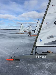 several small sailboats are on the ice with one person walking behind them and another boat in the background