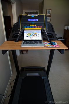 a laptop computer sitting on top of a wooden desk next to a treading machine