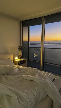 an unmade bed with white sheets and pillows in front of large windows overlooking the city