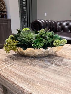 a wooden table topped with a bowl filled with succulents and greenery