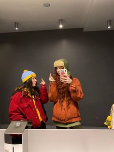 two women standing in front of a counter taking pictures with their cell phones while wearing winter clothing