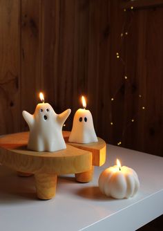 three candles with ghost faces on them sitting on a wooden tray next to pumpkins