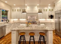 a large kitchen with white cabinets and marble counter tops, two stools at the island