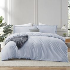 a bed with blue sheets and pillows in a room next to a potted plant