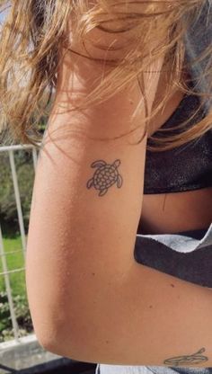 a woman's arm with a small tattoo of a turtle on her left shoulder