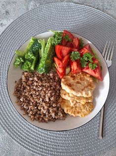 a white plate topped with meat, beans and veggies next to a fork