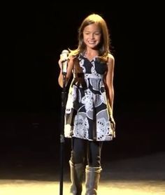 a woman standing on top of a stage with a microphone in her hand and smiling at the camera