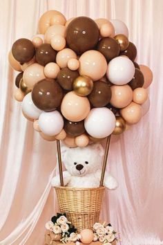 a teddy bear sitting in front of a basket filled with balloons