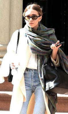 a woman walking down the street while holding onto her cell phone and wearing a scarf