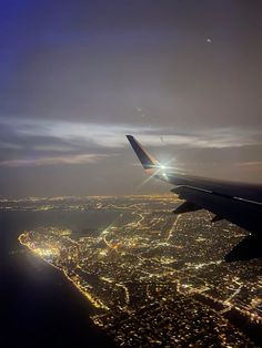 an airplane wing flying over the city lights at night with bright light shining on it