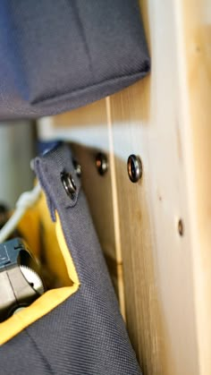 a pair of scissors in a pocket on the side of a wooden shelf with other tools