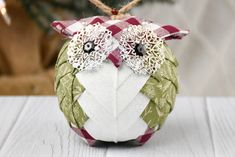 an owl ornament hanging from a christmas tree on a white wooden table with a red and green checkered ribbon