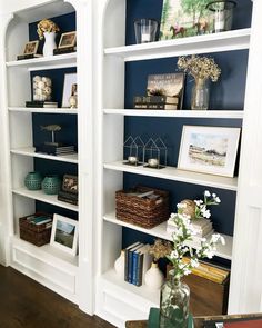 two white bookshelves with blue walls and flowers in vases on the table