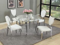 a glass dining table with white chairs and pink flowers in the center on carpeted area