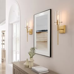 a white hallway with gold sconces and artwork on the wall, along with a large mirror