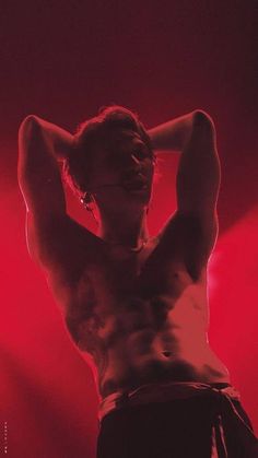 a shirtless man standing in front of a red light with his hands behind his head