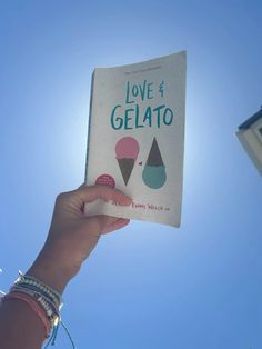 a person holding up a love and gelato book in front of a blue sky