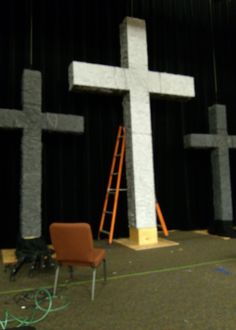 a large white cross sitting on top of a stage next to a chair and ladder