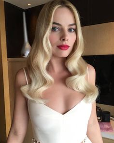 a woman with long blonde hair wearing a white dress and red lipstick is posing for the camera