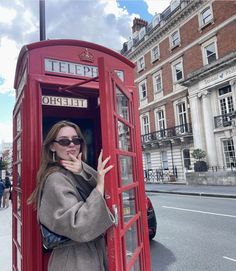 a woman standing in a red phone booth on the side of the road with her hand up