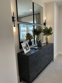 a large mirror is on the wall above a dresser with two vases and plants