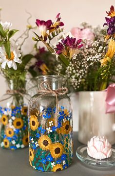 three vases with painted flowers in them sitting on a table next to a glass plate